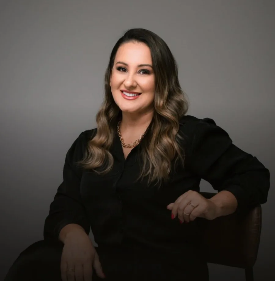 Alessandra Rodrigues sorrindo, de blazer preto, sentada
